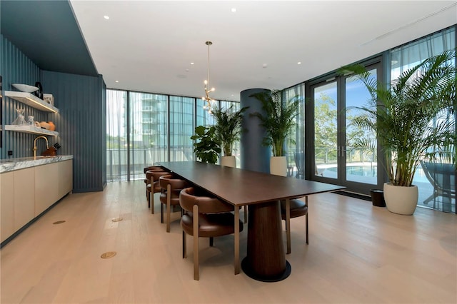 dining room featuring light wood-type flooring, a notable chandelier, and a wall of windows