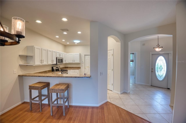 kitchen featuring white cabinets, dark stone counters, light hardwood / wood-style floors, kitchen peninsula, and stainless steel appliances