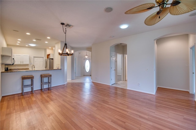 kitchen with pendant lighting, stainless steel refrigerator, white cabinets, light hardwood / wood-style floors, and kitchen peninsula