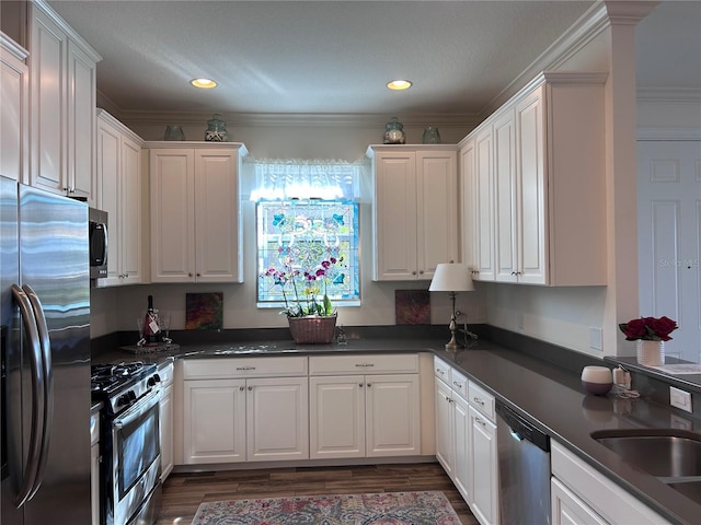 kitchen with white cabinets, dark wood finished floors, dark countertops, stainless steel appliances, and crown molding