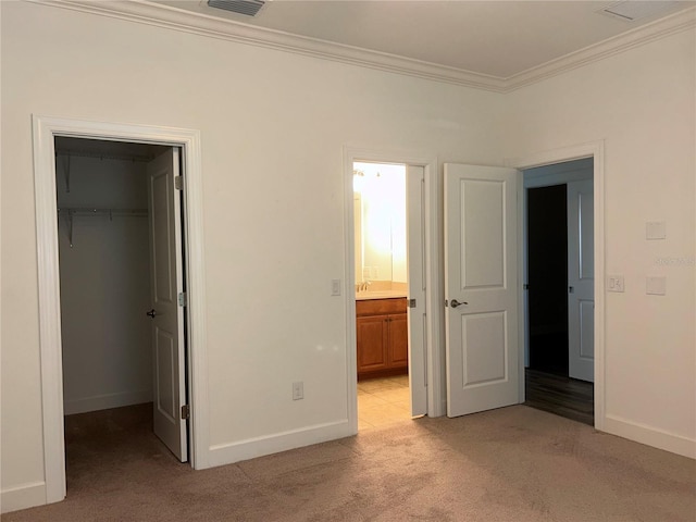 unfurnished bedroom with light carpet, baseboards, ornamental molding, a closet, and a walk in closet