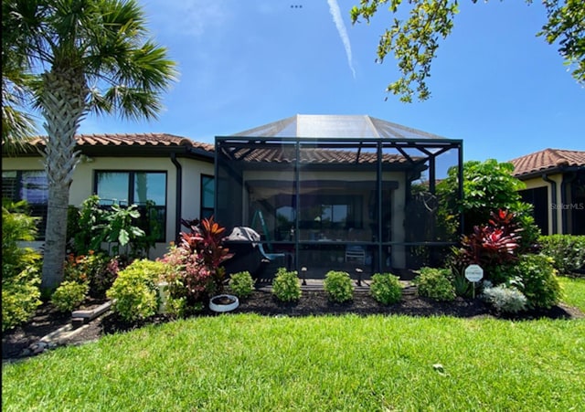 back of house featuring a lanai, a tile roof, a lawn, and stucco siding