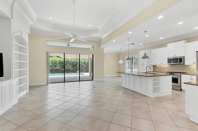 kitchen with built in shelves, decorative light fixtures, a center island with sink, appliances with stainless steel finishes, and white cabinets