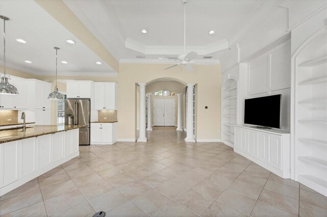 unfurnished living room featuring crown molding, light tile patterned flooring, built in shelves, a raised ceiling, and ornate columns