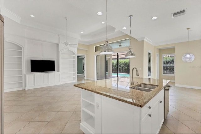 kitchen featuring sink, stone counters, white cabinets, a center island with sink, and built in shelves