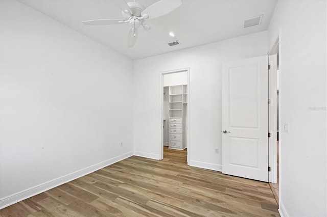 unfurnished bedroom with hardwood / wood-style floors, a walk in closet, a closet, and ceiling fan