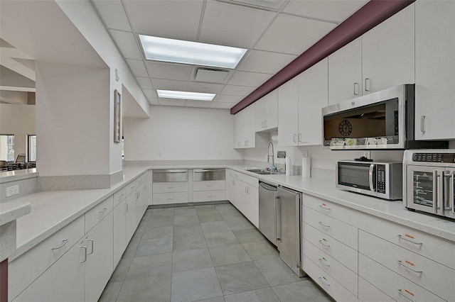 kitchen with appliances with stainless steel finishes, light tile patterned floors, white cabinets, and a paneled ceiling