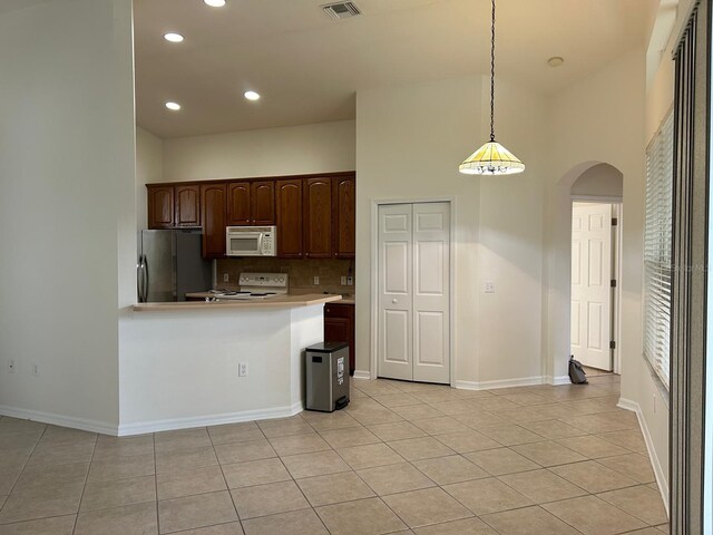 kitchen with light tile patterned floors, a towering ceiling, decorative backsplash, stainless steel fridge, and stove