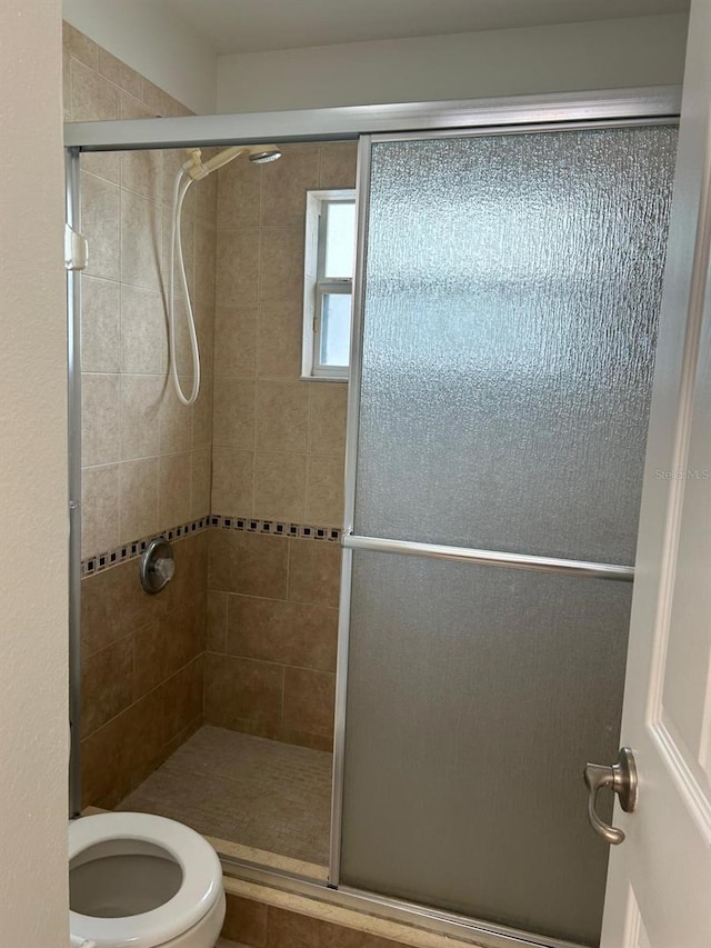 bathroom featuring a shower with door and toilet