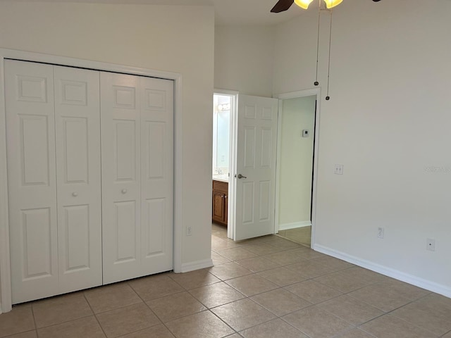 unfurnished bedroom with light tile patterned flooring, a closet, ceiling fan, and connected bathroom