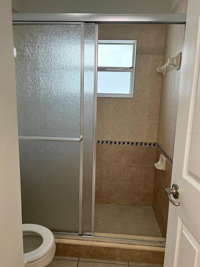 bathroom featuring tile patterned flooring, a shower with shower door, and toilet