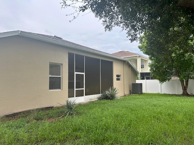 rear view of property featuring central AC unit and a lawn