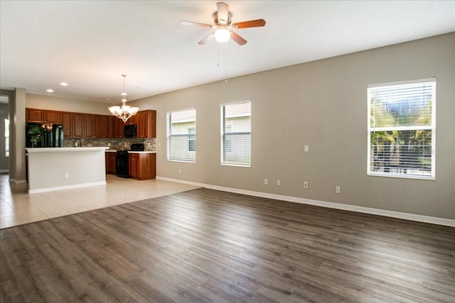 unfurnished living room with ceiling fan with notable chandelier and wood-type flooring