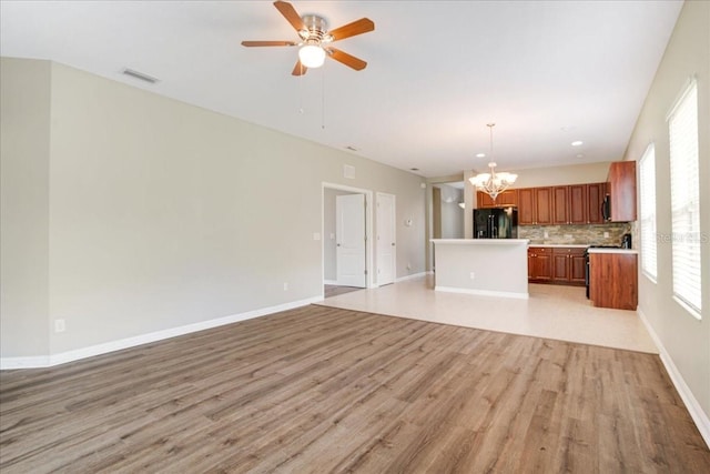 unfurnished living room featuring a wealth of natural light, ceiling fan with notable chandelier, and light hardwood / wood-style flooring