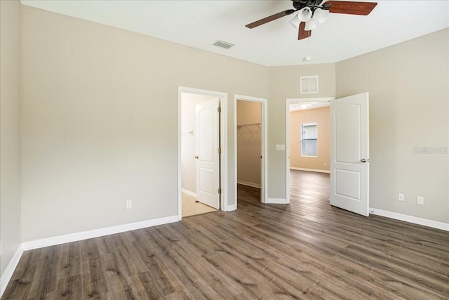 unfurnished bedroom featuring ceiling fan, a closet, a spacious closet, and dark wood-type flooring