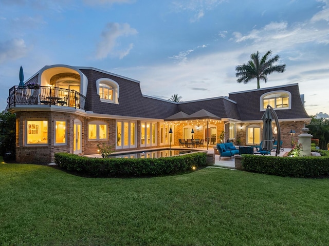 back house at dusk with a lawn, a balcony, an outdoor hangout area, and a patio