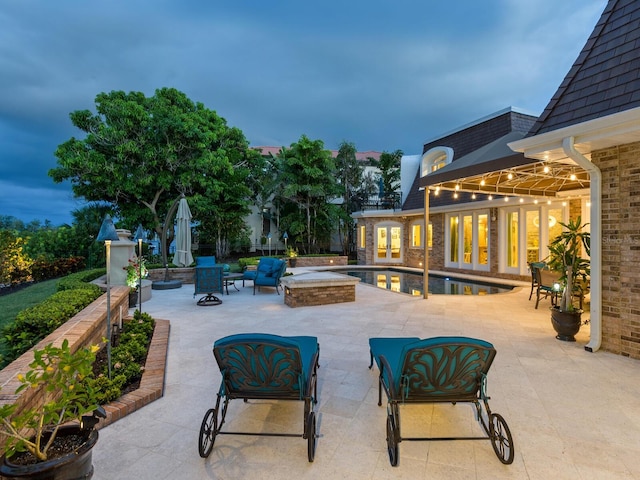 patio terrace at dusk with a swimming pool with hot tub and an outdoor living space with a fire pit