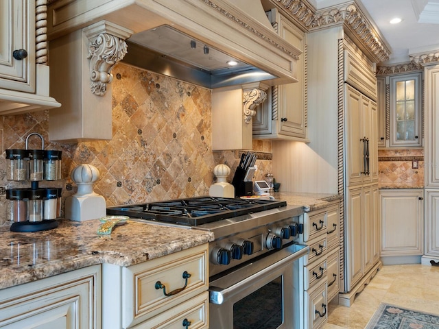 kitchen with light stone countertops, crown molding, high end range, and cream cabinetry