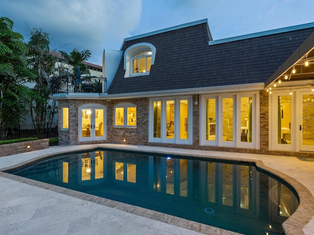 back house at dusk with french doors and a balcony