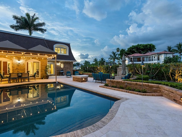 pool at dusk featuring a patio area and exterior fireplace