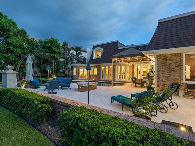 back house at dusk with an outdoor living space with a fire pit and a patio