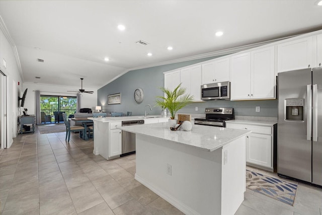 kitchen featuring ceiling fan, stainless steel appliances, ornamental molding, a center island, and light stone counters