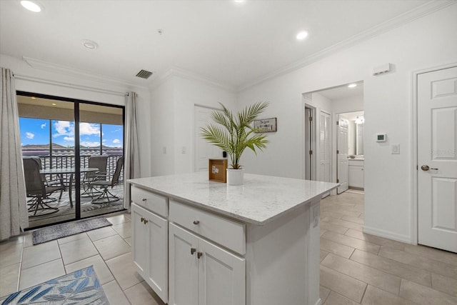 kitchen featuring light stone counters, light tile patterned floors, a center island, white cabinetry, and ornamental molding