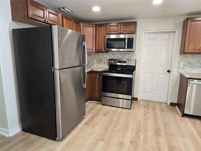 kitchen featuring tasteful backsplash, light hardwood / wood-style floors, light stone counters, and stainless steel appliances