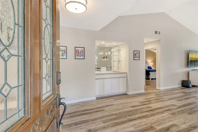 foyer entrance with a textured ceiling, light hardwood / wood-style flooring, and vaulted ceiling