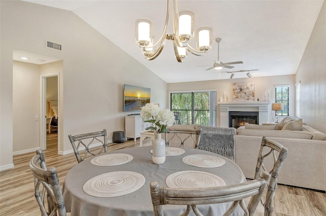 dining area with light hardwood / wood-style flooring, ceiling fan with notable chandelier, rail lighting, and high vaulted ceiling