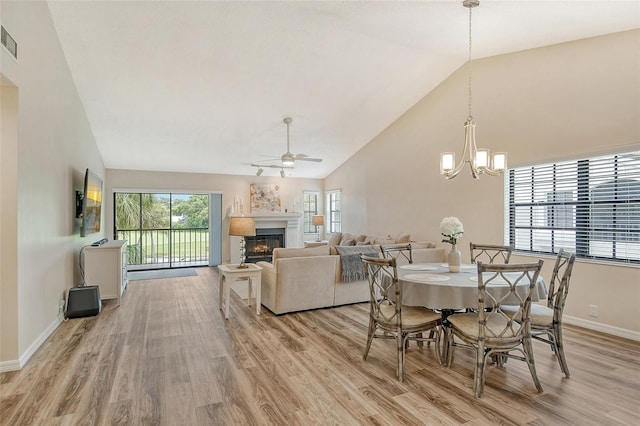 dining room with light hardwood / wood-style floors, ceiling fan with notable chandelier, and high vaulted ceiling