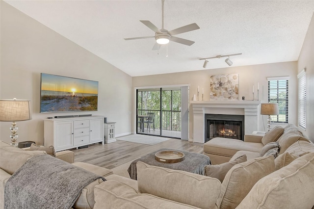 living room with light hardwood / wood-style floors, rail lighting, a textured ceiling, lofted ceiling, and ceiling fan