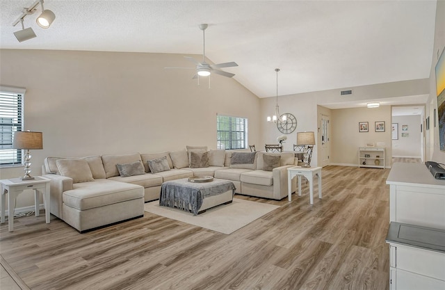 living room featuring ceiling fan with notable chandelier, light hardwood / wood-style floors, a textured ceiling, and high vaulted ceiling