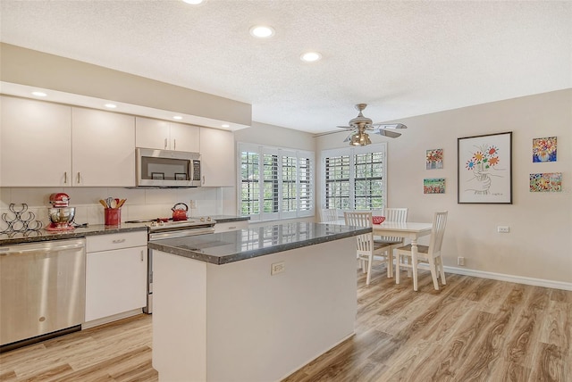 kitchen featuring light hardwood / wood-style flooring, dark stone counters, a center island, ceiling fan, and appliances with stainless steel finishes