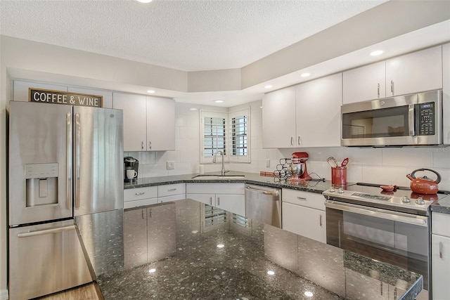 kitchen with white cabinetry, dark stone countertops, tasteful backsplash, appliances with stainless steel finishes, and sink