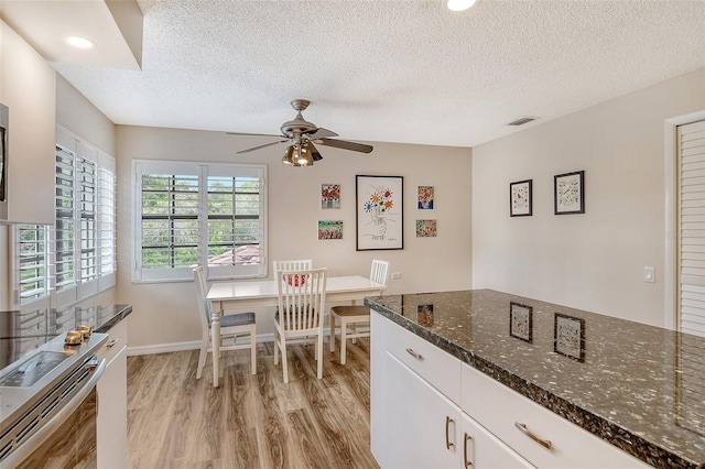 kitchen with dark stone counters, ceiling fan, white cabinets, light hardwood / wood-style floors, and a textured ceiling