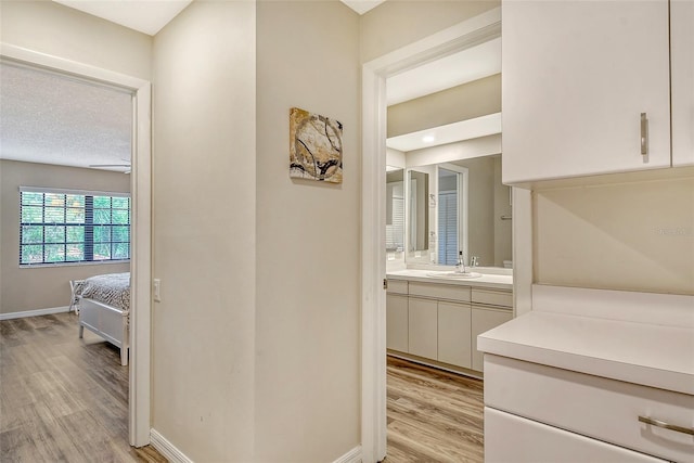 corridor featuring sink, a textured ceiling, and light wood-type flooring