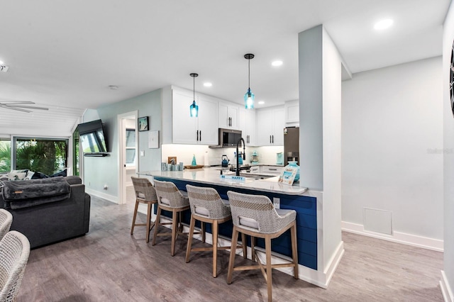 kitchen with a kitchen bar, white cabinetry, hanging light fixtures, kitchen peninsula, and stainless steel appliances