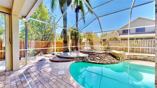 view of pool with an in ground hot tub, a patio area, and glass enclosure