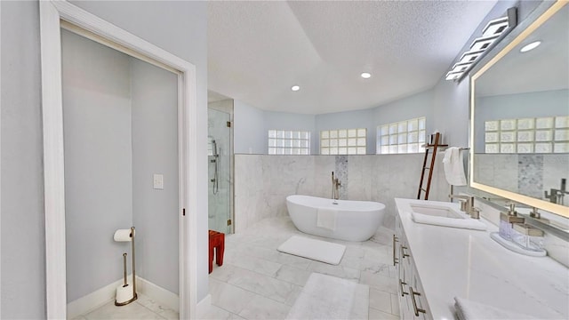 bathroom with plus walk in shower, tile walls, vanity, and a textured ceiling