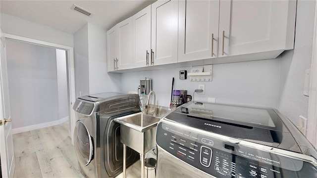 clothes washing area featuring cabinets, washer and clothes dryer, and light wood-type flooring