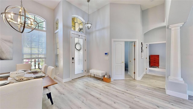 entrance foyer with a notable chandelier, a towering ceiling, light hardwood / wood-style floors, and ornate columns