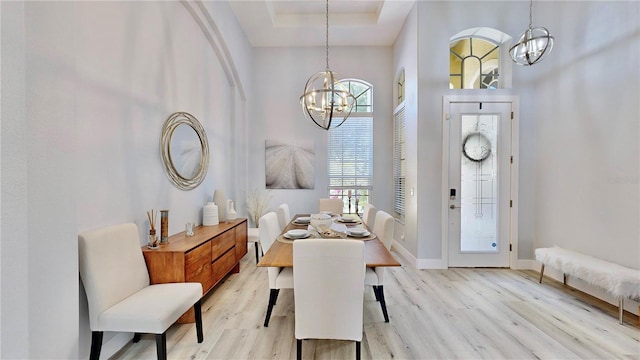 dining space with a tray ceiling, a notable chandelier, and light hardwood / wood-style flooring