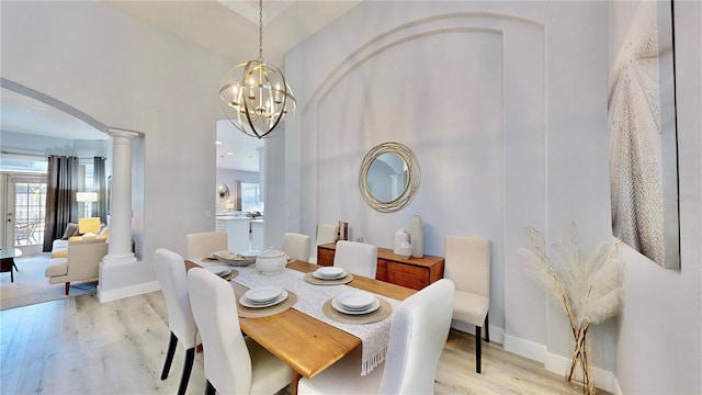 dining space with decorative columns, an inviting chandelier, and light wood-type flooring