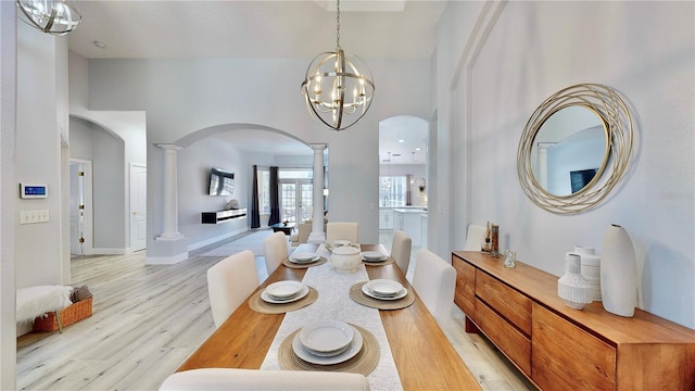 dining area featuring a towering ceiling, decorative columns, light hardwood / wood-style flooring, and a notable chandelier