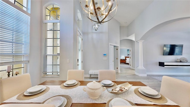 dining room with a towering ceiling, light hardwood / wood-style floors, a chandelier, and ornate columns