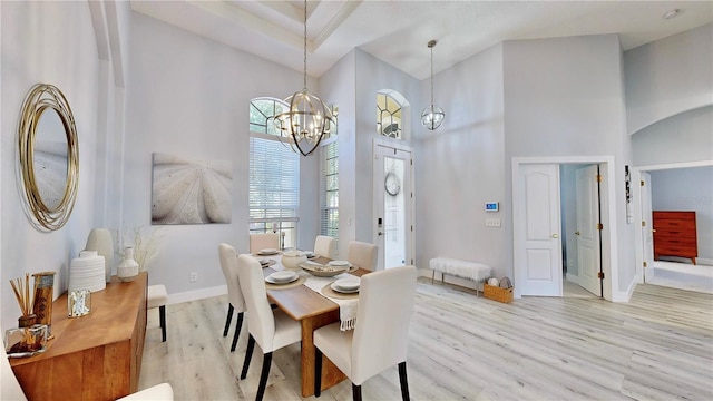 dining space with a towering ceiling, a chandelier, and light wood-type flooring