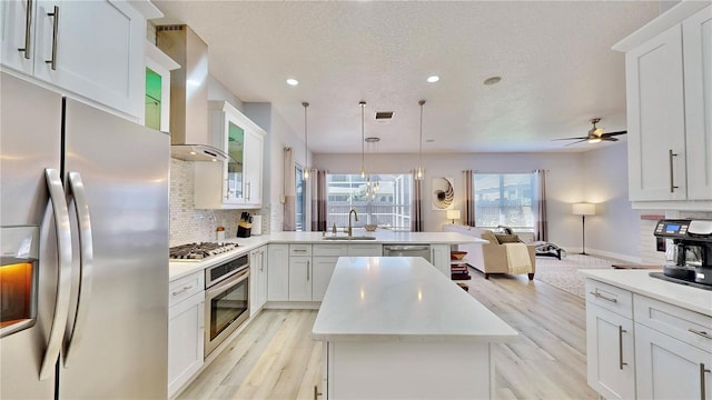 kitchen with white cabinetry, stainless steel appliances, sink, and wall chimney range hood