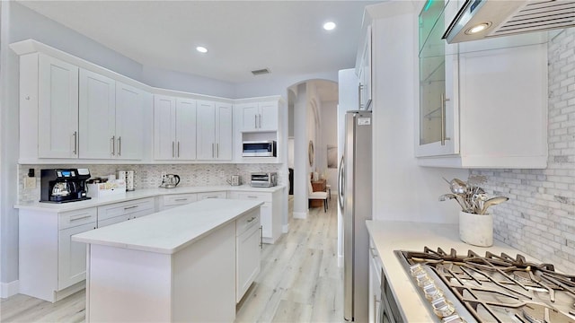 kitchen with white cabinetry, backsplash, range hood, and appliances with stainless steel finishes