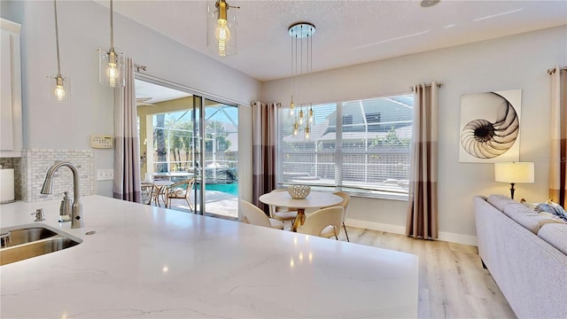 kitchen featuring sink, tasteful backsplash, pendant lighting, light stone countertops, and light hardwood / wood-style floors